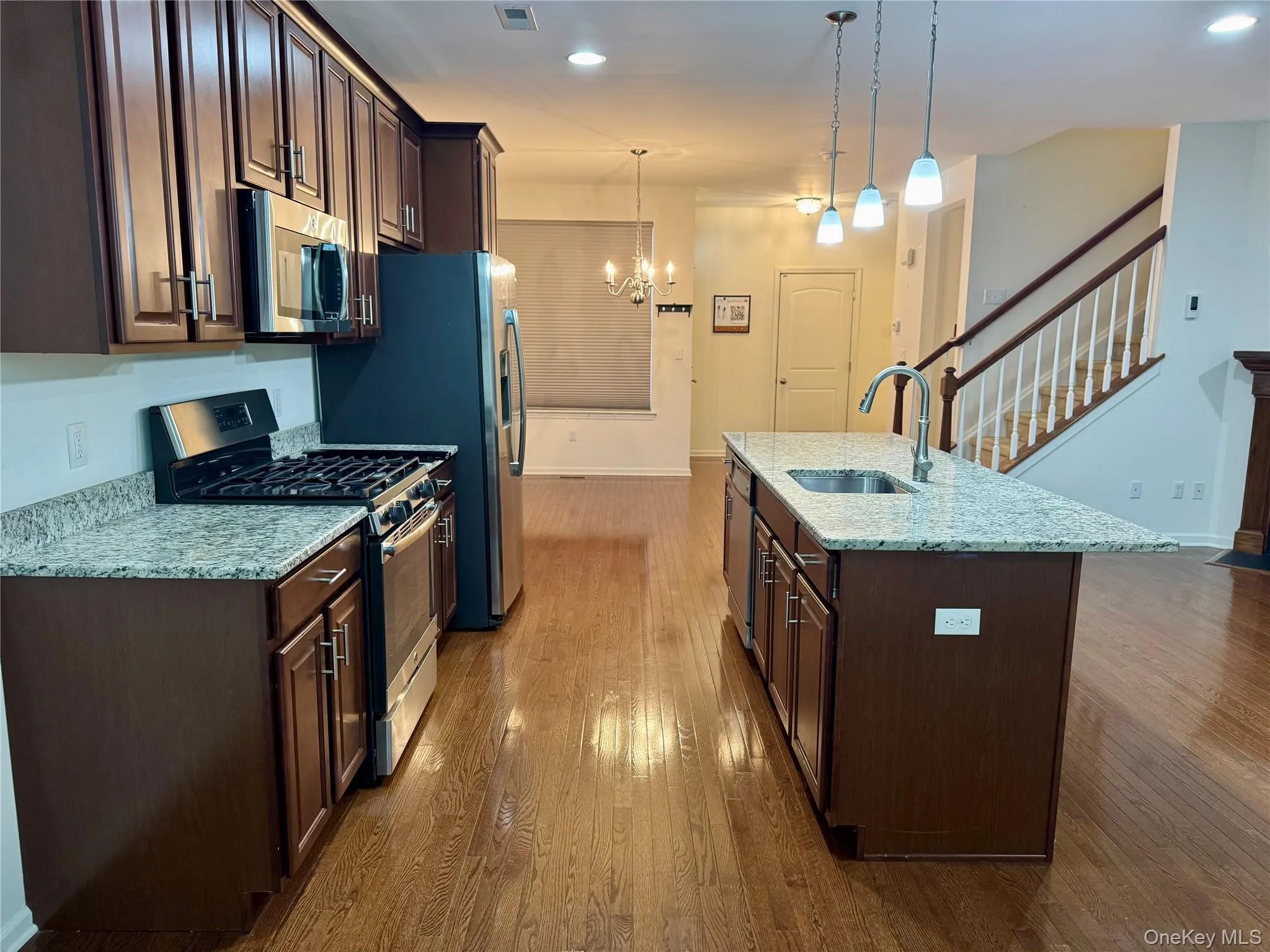 Kitchen with stainless steel appliances, dark wood-type flooring, dark brown cabinetry, a chandelier, and an island with sink Kitchen with stainless steel appliances, dark wood-type flooring, dark brown cabinetry, a chandelier, and an island with sink