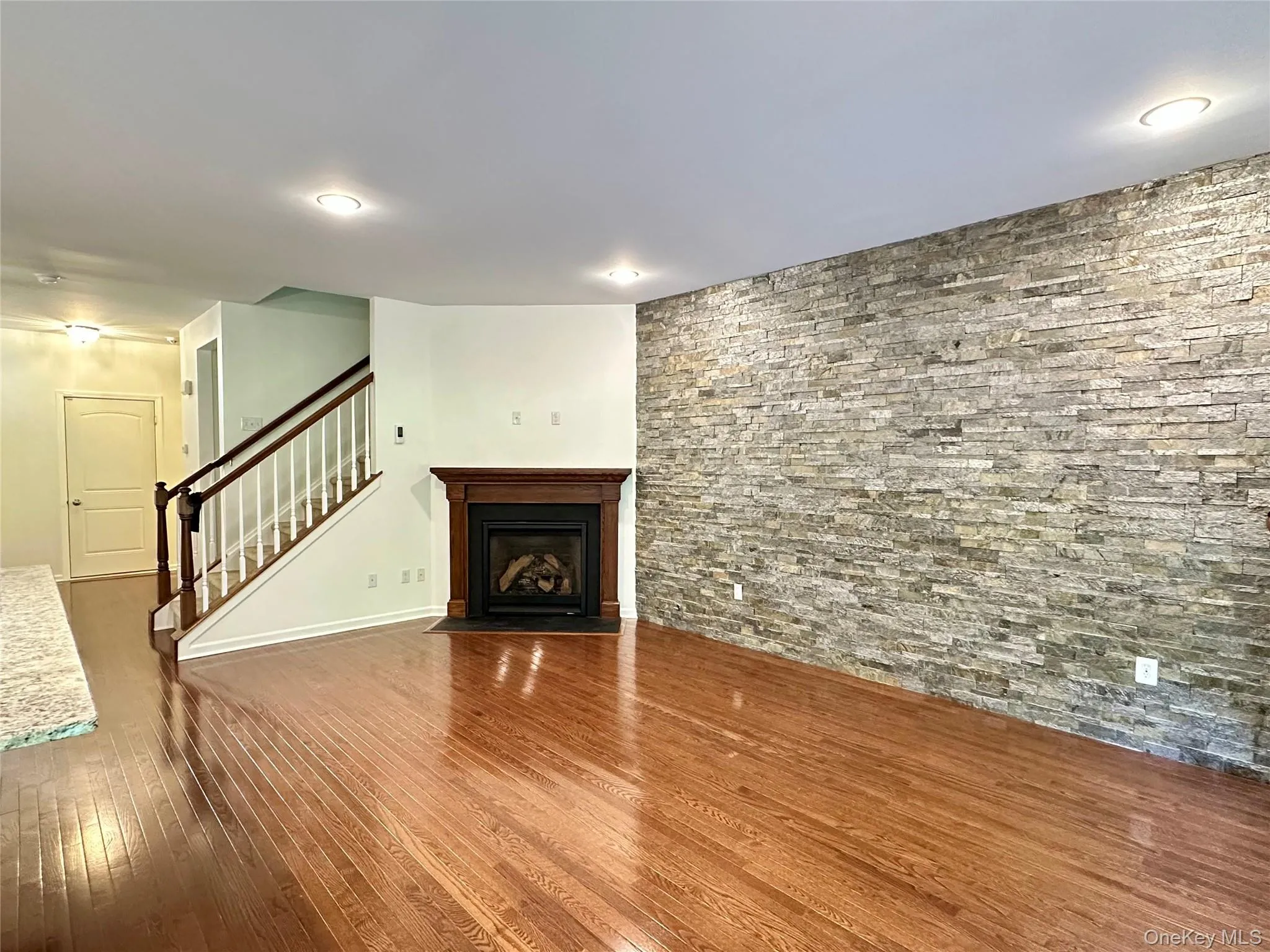 Unfurnished living room with stairs, hardwood / wood-style floors, and a fireplace with flush hearth Unfurnished living room with stairs, hardwood / wood-style floors, and a fireplace with flush hearth