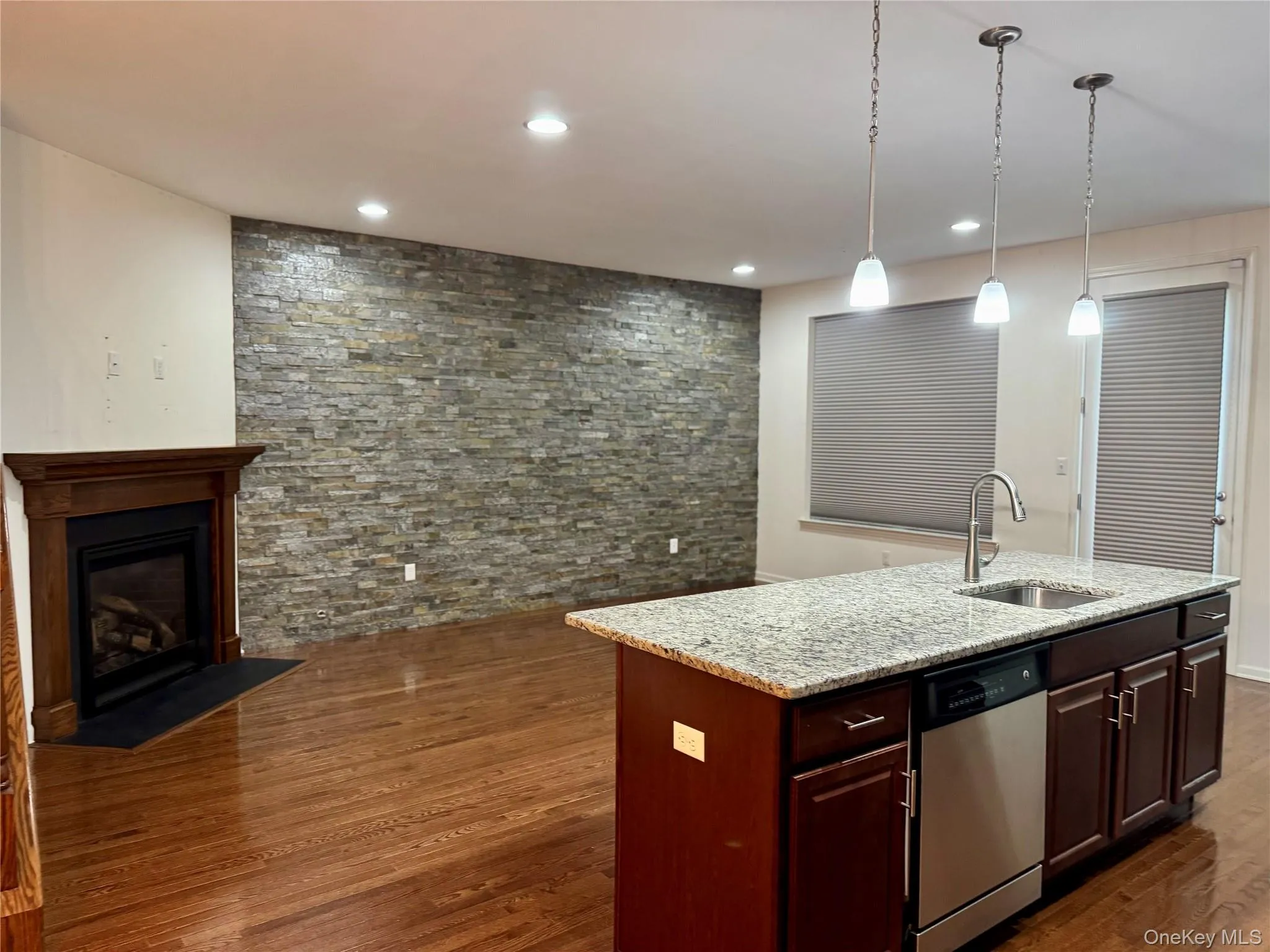 Kitchen with dishwasher, dark wood-type flooring, an island with sink, light stone countertops, and decorative light fixtures Kitchen with dishwasher, dark wood-type flooring, an island with sink, light stone countertops, and decorative light fixtures