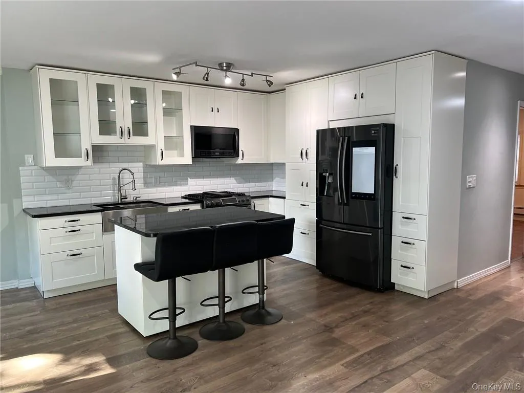 Kitchen with decorative backsplash, white cabinets, black appliances, and a kitchen bar Kitchen with decorative backsplash, white cabinets, black appliances, and a kitchen bar