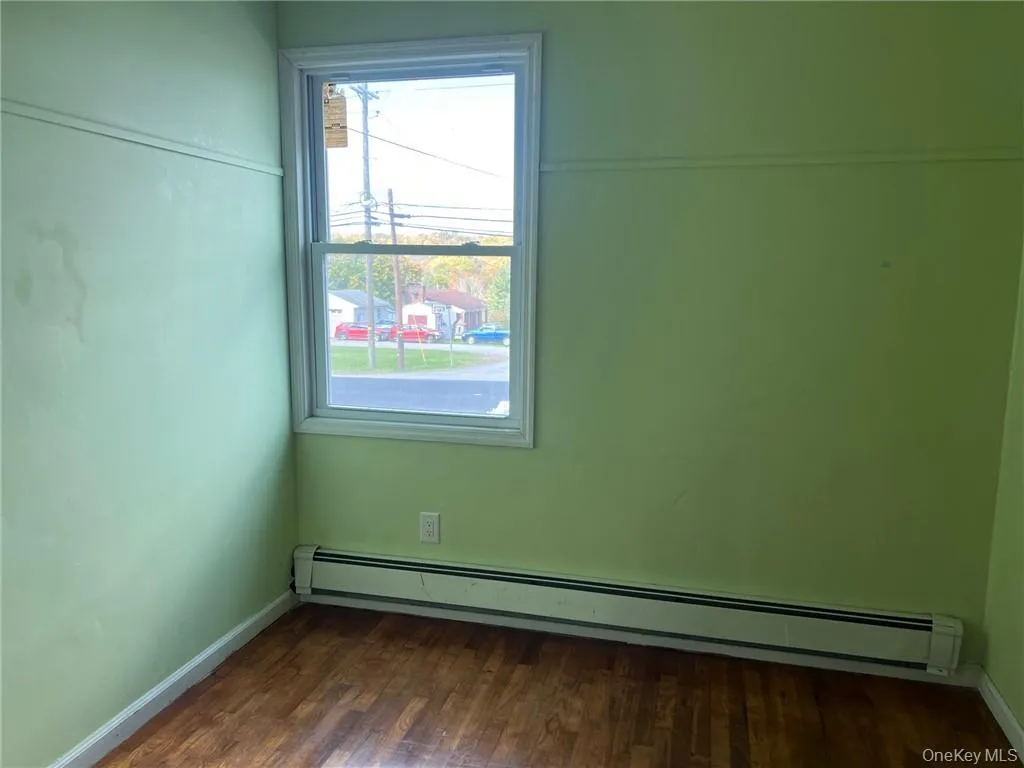 Empty room featuring dark hardwood / wood-style floors and baseboard heating Empty room featuring dark hardwood / wood-style floors and baseboard heating