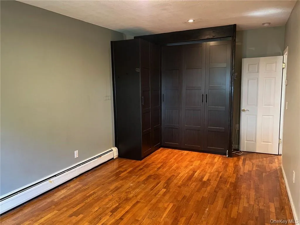 Unfurnished bedroom featuring a closet, baseboard heating, light wood-type flooring, and a textured ceiling Unfurnished bedroom featuring a closet, baseboard heating, light wood-type flooring, and a textured ceiling