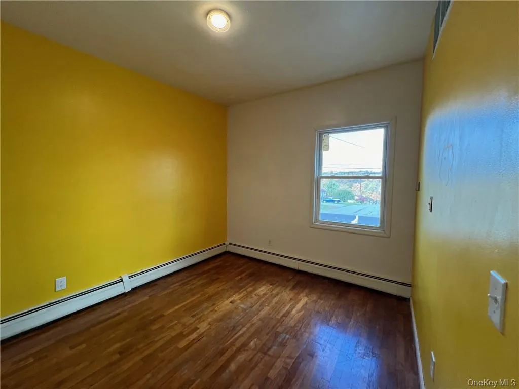 Unfurnished bedroom featuring dark wood-type flooring and a baseboard radiator Unfurnished bedroom featuring dark wood-type flooring and a baseboard radiator