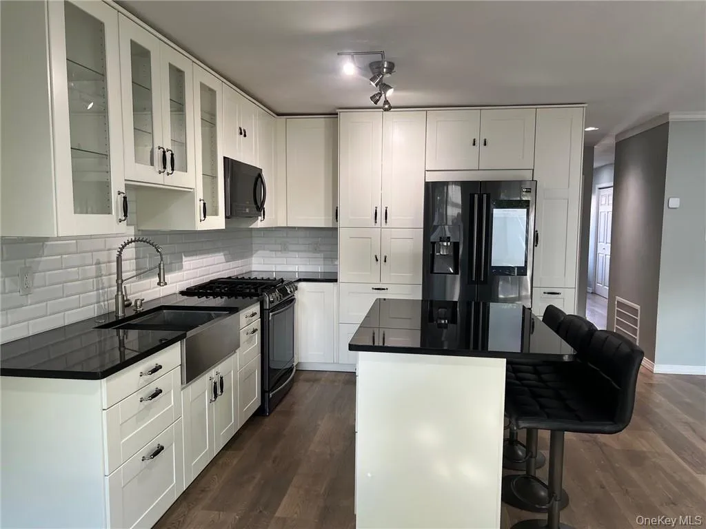 Kitchen featuring sink, dark wood-type flooring, white cabinetry, black appliances, and a breakfast bar Kitchen featuring sink, dark wood-type flooring, white cabinetry, black appliances, and a breakfast bar
