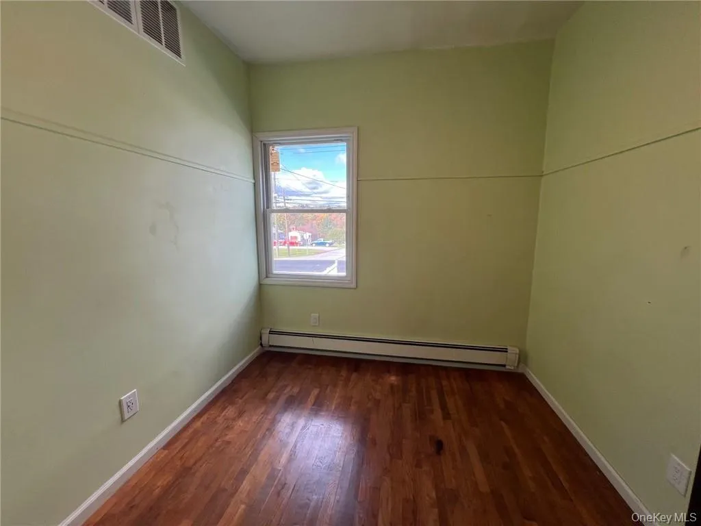 Unfurnished room with dark wood-type flooring and a baseboard radiator Unfurnished room with dark wood-type flooring and a baseboard radiator