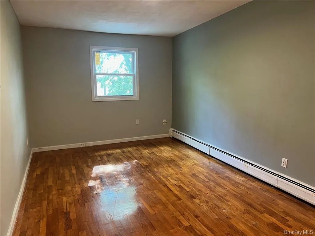 Unfurnished room featuring dark wood-type flooring and a baseboard radiator Unfurnished room featuring dark wood-type flooring and a baseboard radiator