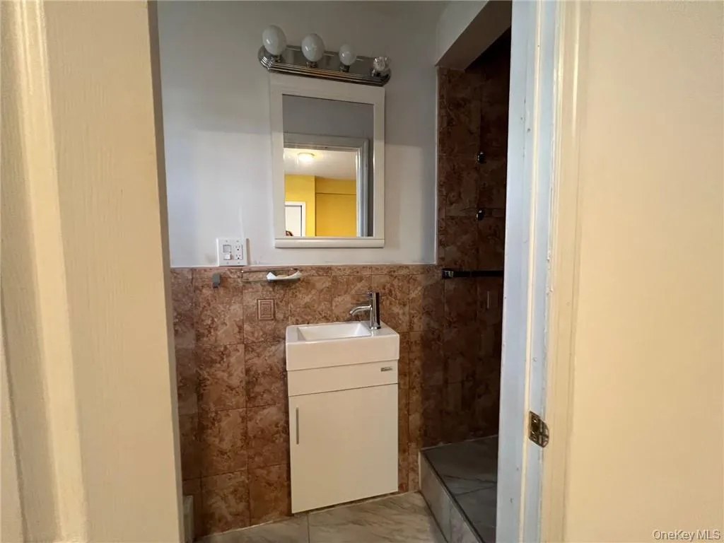 Bathroom featuring a shower, vanity, and tile walls Bathroom featuring a shower, vanity, and tile walls