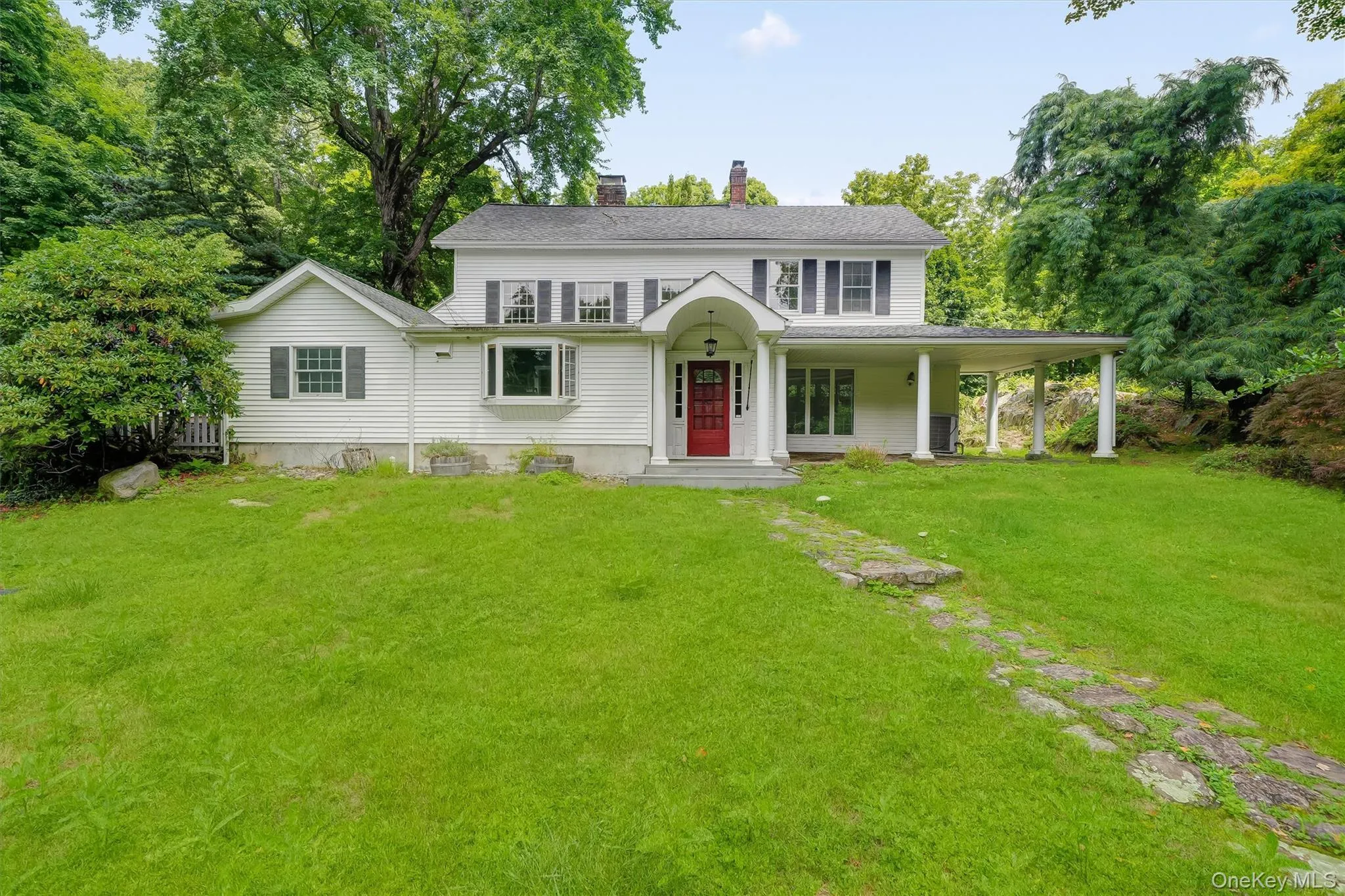 White siding exterior with a red entry door, covered front porch, bay window, and a stone pathway White siding exterior with a red entry door, covered front porch, bay window, and a stone pathway