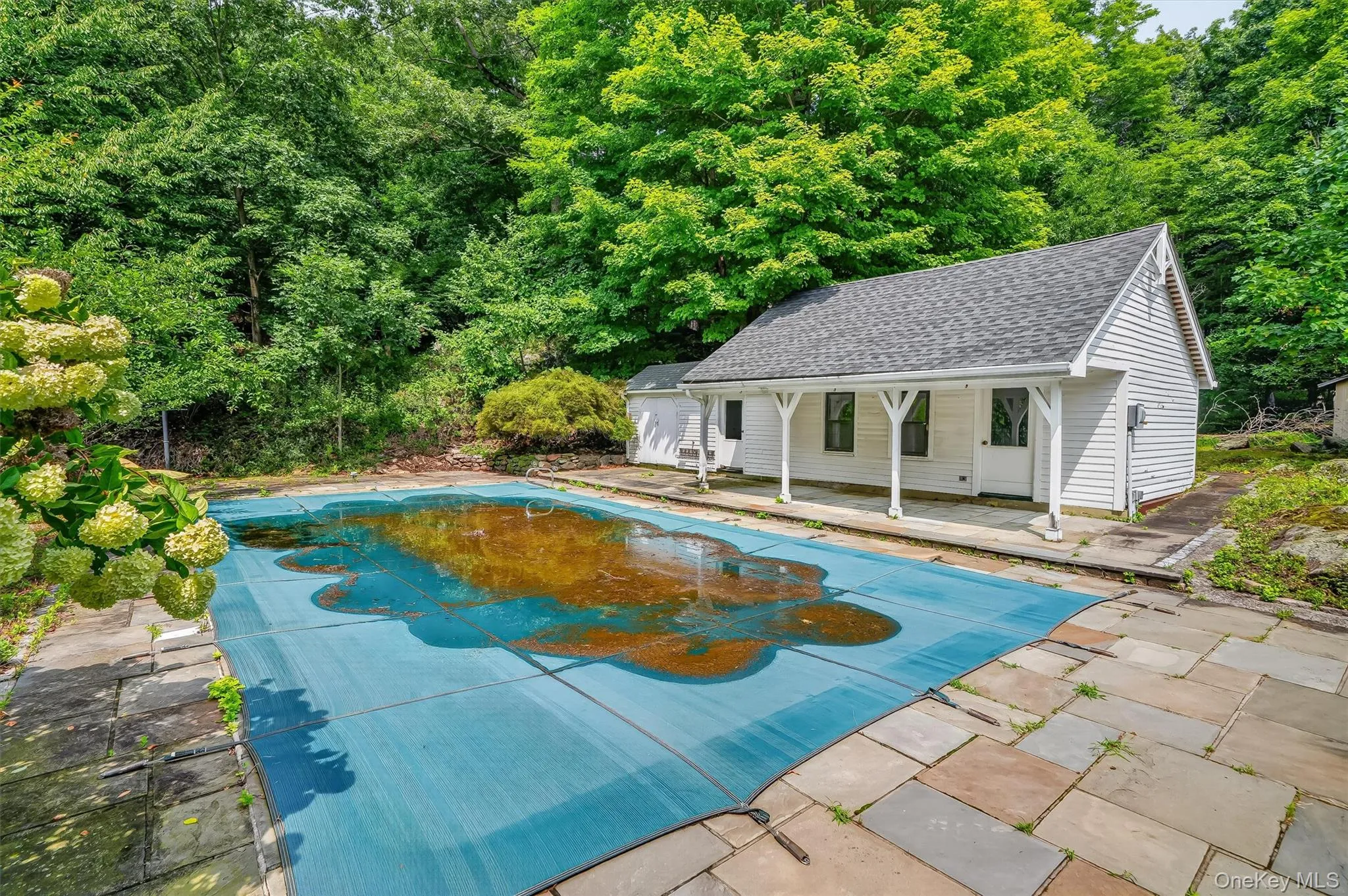 In-ground pool with protective cover, stone patio, and a cabana featuring a covered porch with white columns In-ground pool with protective cover, stone patio, and a cabana featuring a covered porch with white columns