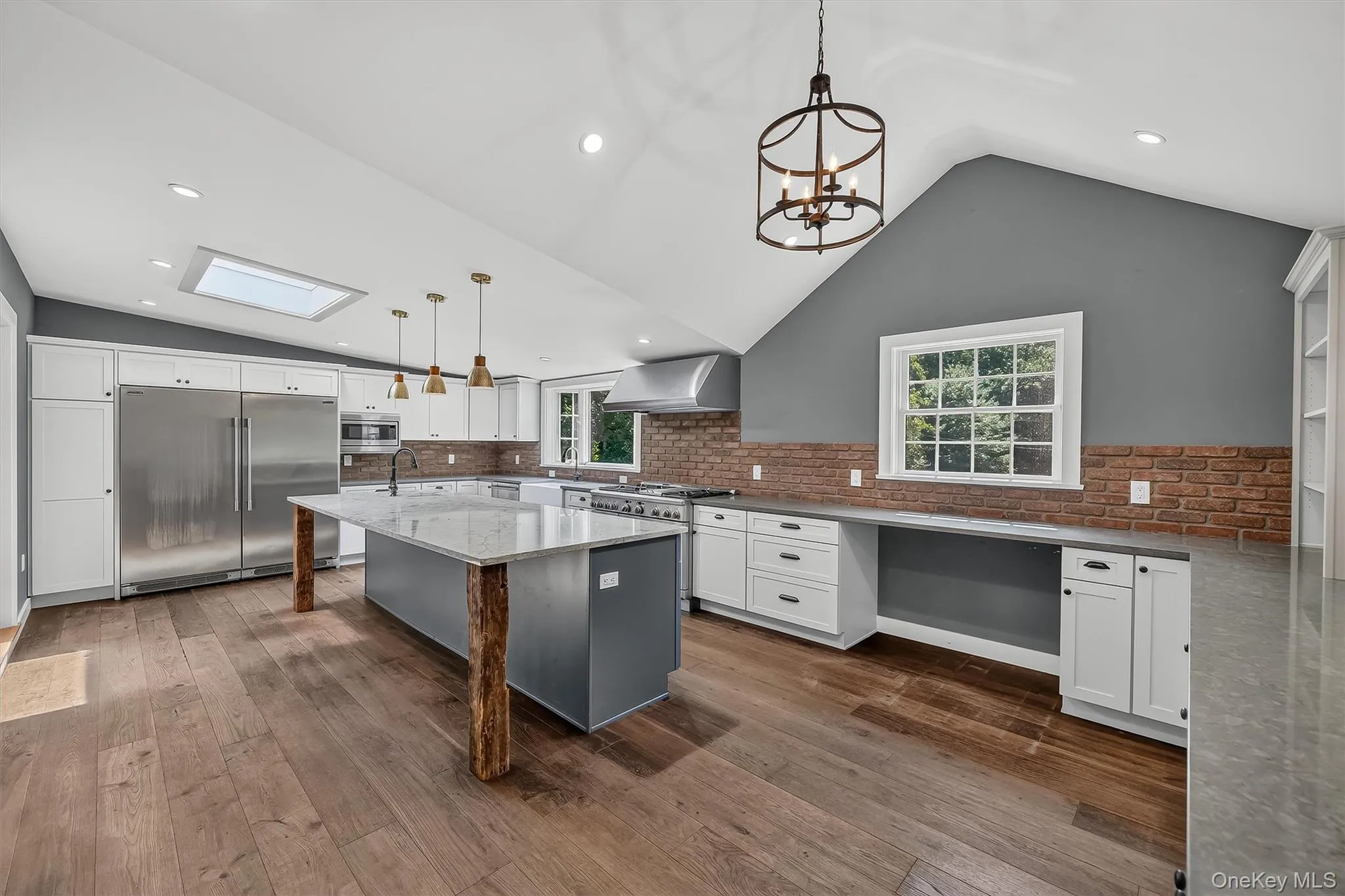 Vaulted ceiling kitchen featuring wood-finish flooring, a skylight, and an expansive island with a stone countertop. Plank Floor, Commercial grade kitchen appliances Vaulted ceiling kitchen featuring wood-finish flooring, a skylight, and an expansive island with a stone countertop. Plank Floor, Commercial grade kitchen appliances