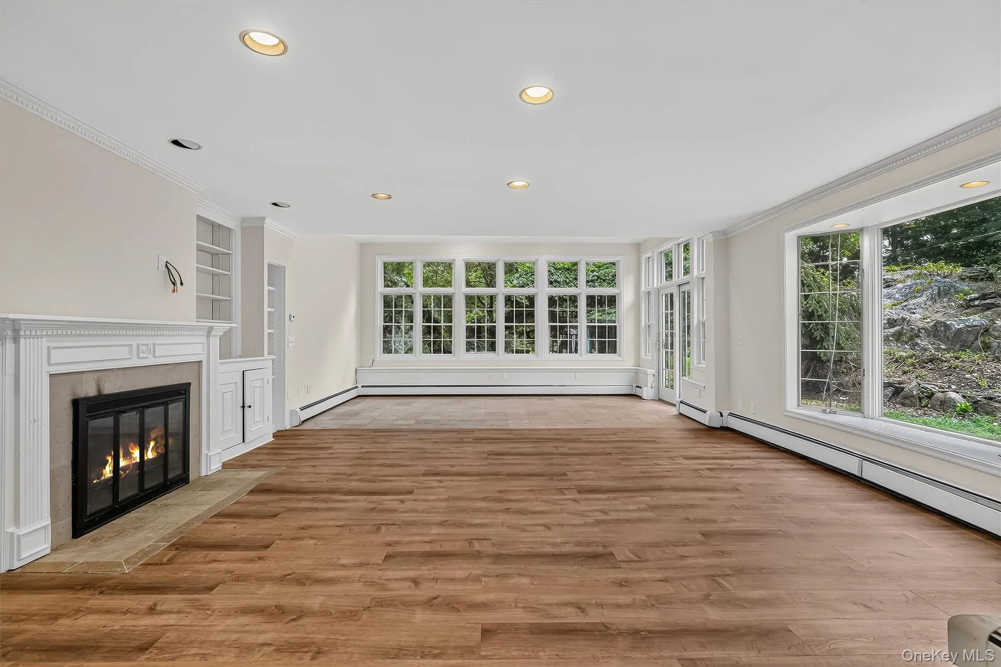 Wood-finish flooring, recessed lighting, and a white mantel fireplace with a stone hearth Wood-finish flooring, recessed lighting, and a white mantel fireplace with a stone hearth