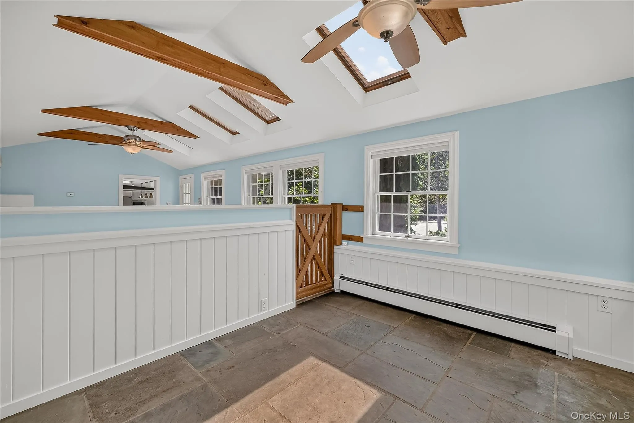Vaulted ceiling with exposed wood beams, multiple skylights, flagstone flooring, paneled wainscoting, and large windows Vaulted ceiling with exposed wood beams, multiple skylights, flagstone flooring, paneled wainscoting, and large windows