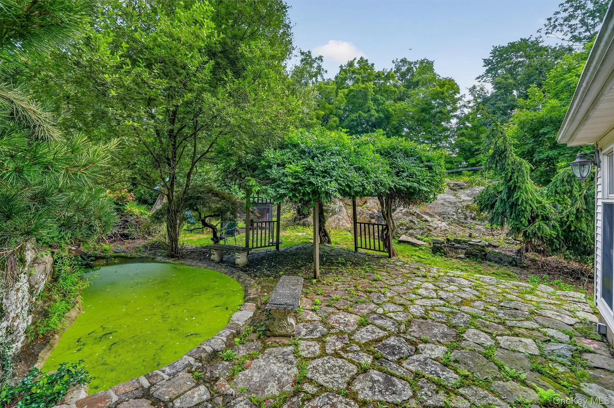 Stone paver patio with natural rock accents, surrounded by mature trees and lush landscaping Stone paver patio with natural rock accents, surrounded by mature trees and lush landscaping