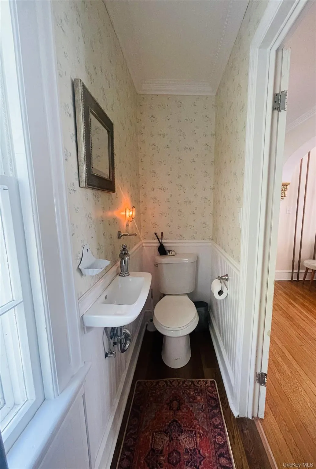 Half bath with crown molding, toilet, wallpapered walls, and wood finished floors Half bath with crown molding, toilet, wallpapered walls, and wood finished floors