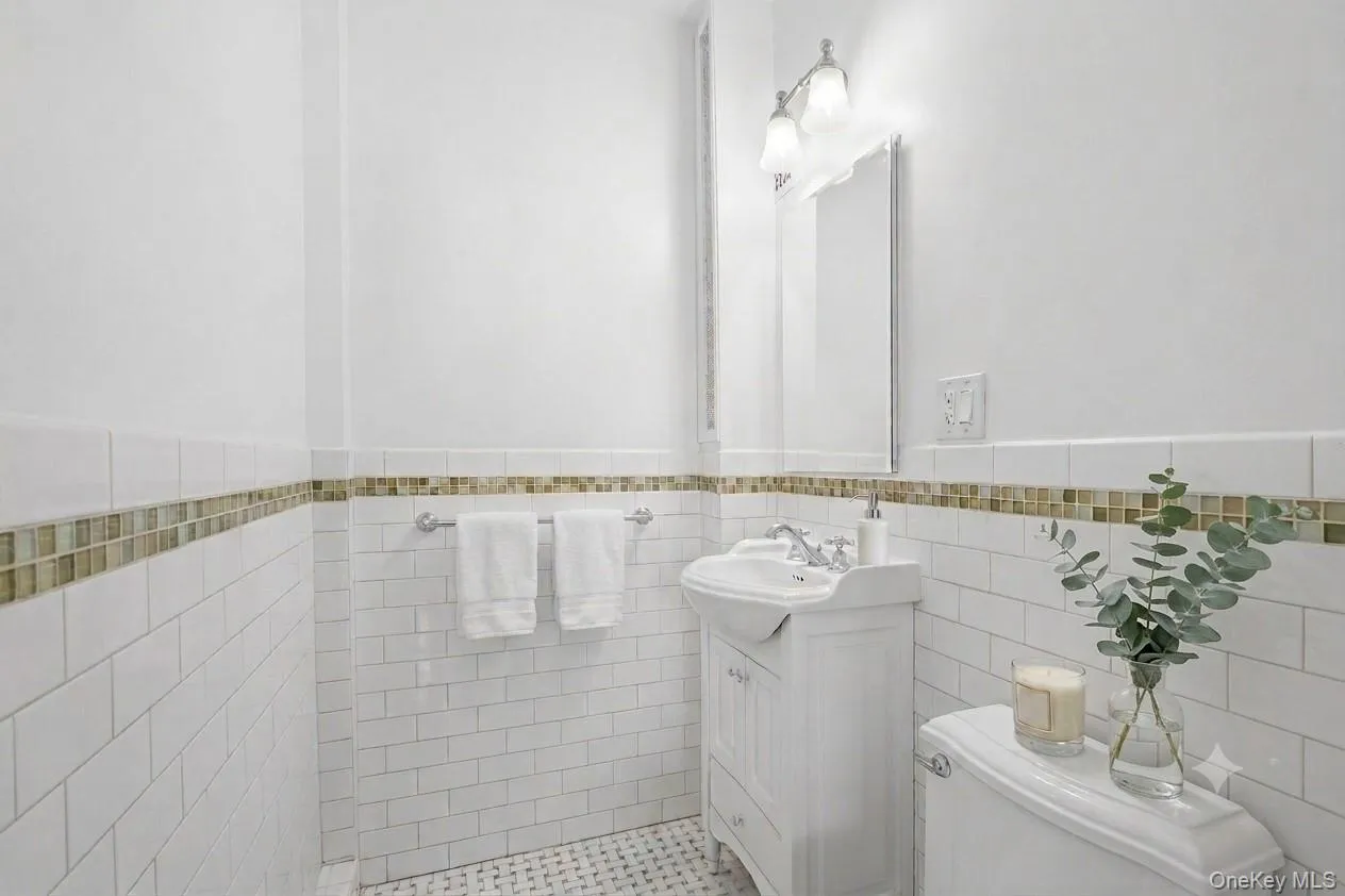 Timeless in design, the primary bath features white subway tile with a mosaic accent band, a white vanity with an integrated sink, chrome fixtures, a wall-mounted mirror, and a walk-in shower. Timeless in design, the primary bath features white subway tile with a mosaic accent band, a white vanity with an integrated sink, chrome fixtures, a wall-mounted mirror, and a walk-in shower.