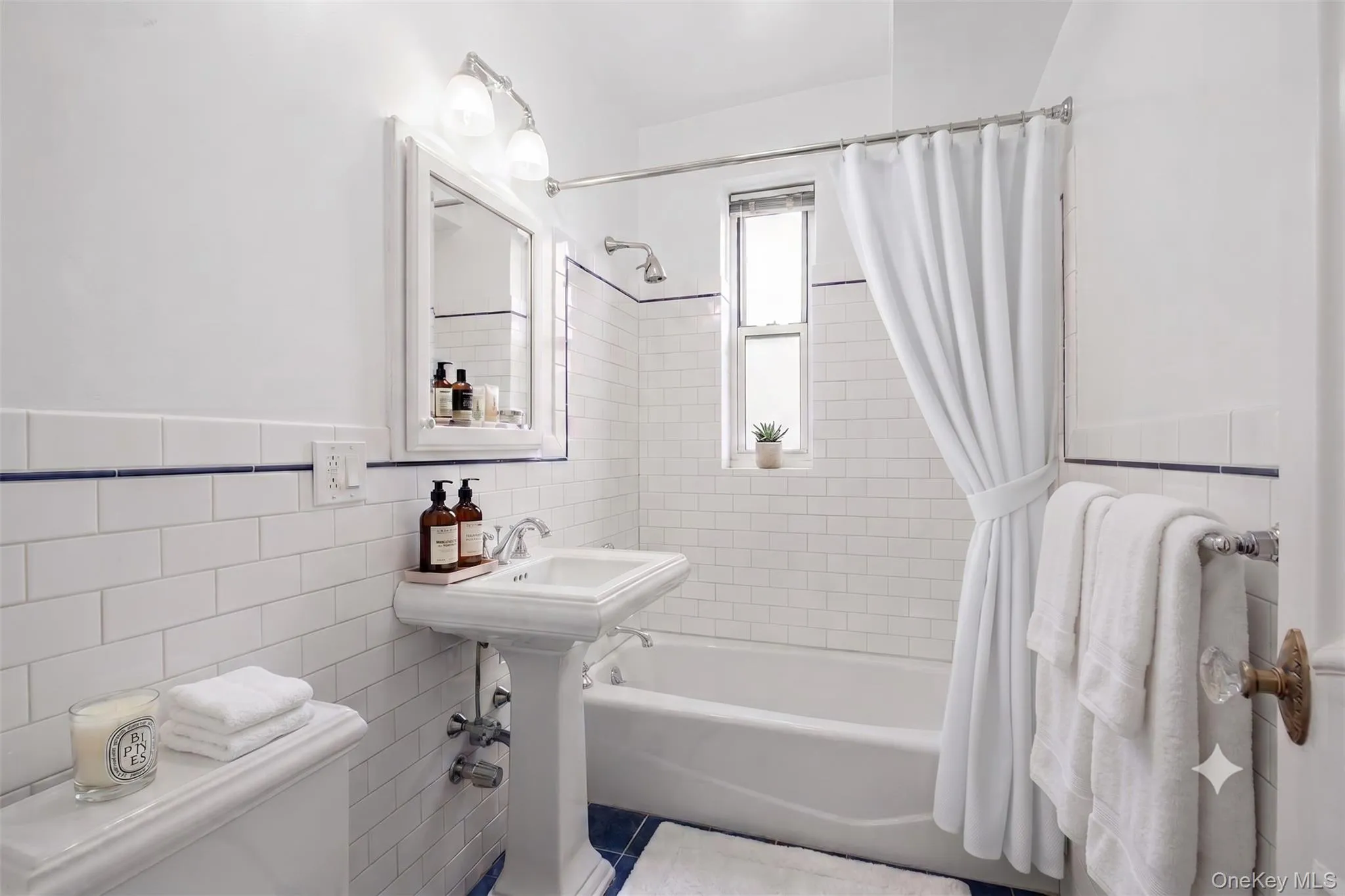 A crisp palette of white subway tile, navy trim, a pedestal sink, and a white tub gives the hall bath enduring appeal. A crisp palette of white subway tile, navy trim, a pedestal sink, and a white tub gives the hall bath enduring appeal.