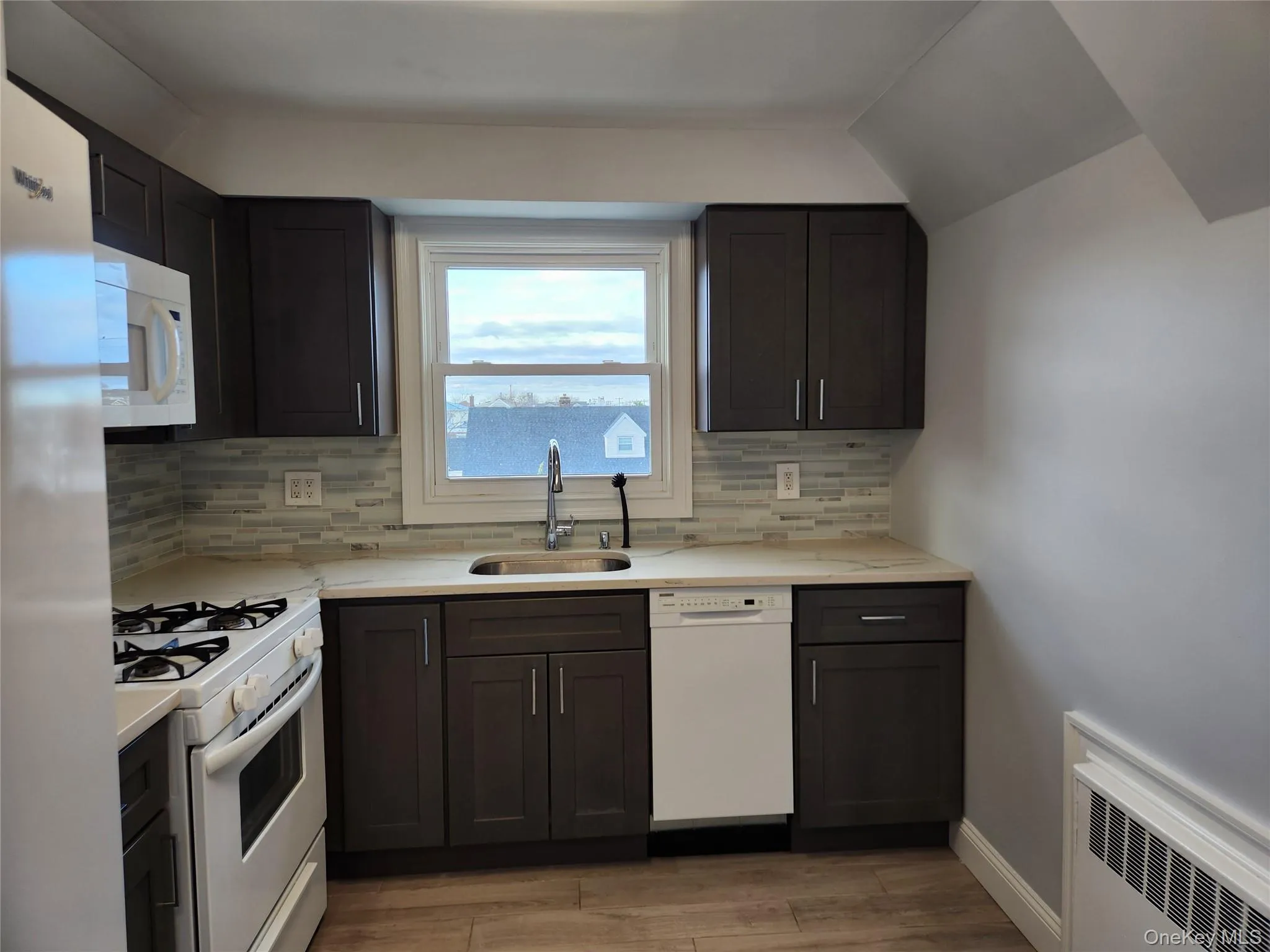 Kitchen with a sink, white appliances, light wood-style floors, radiator, and backsplash Kitchen with a sink, white appliances, light wood-style floors, radiator, and backsplash