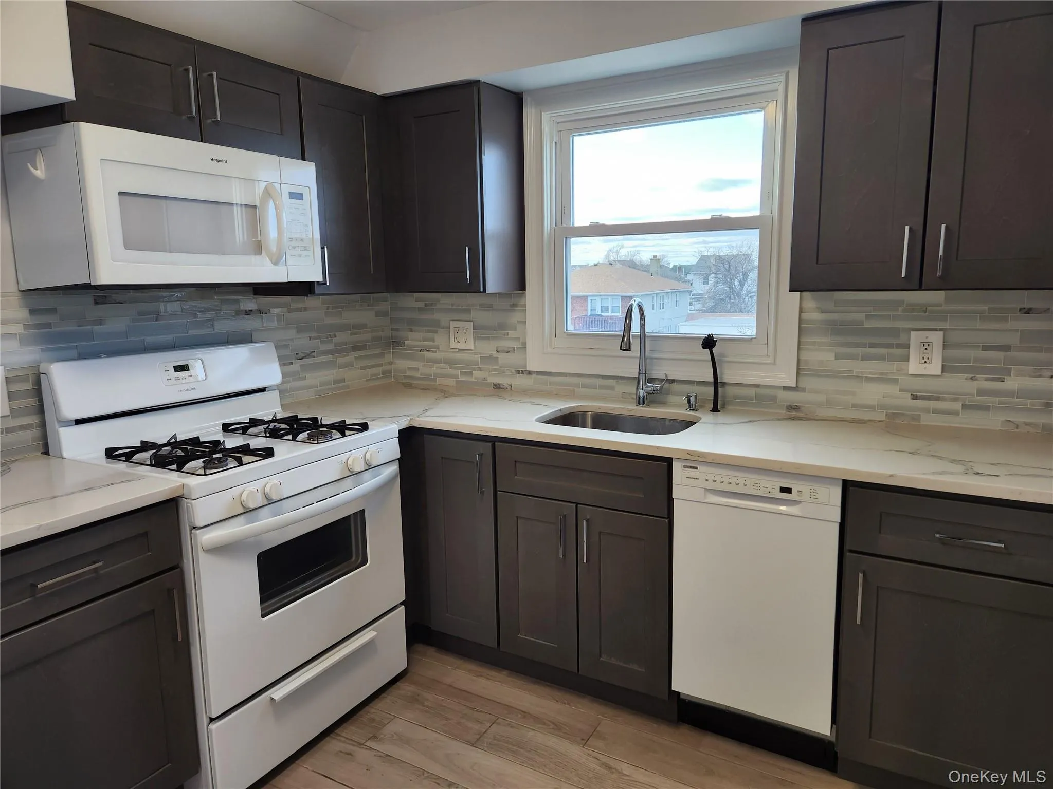 Kitchen with tasteful backsplash, light stone counters, white appliances, light wood-style flooring, and a sink Kitchen with tasteful backsplash, light stone counters, white appliances, light wood-style flooring, and a sink