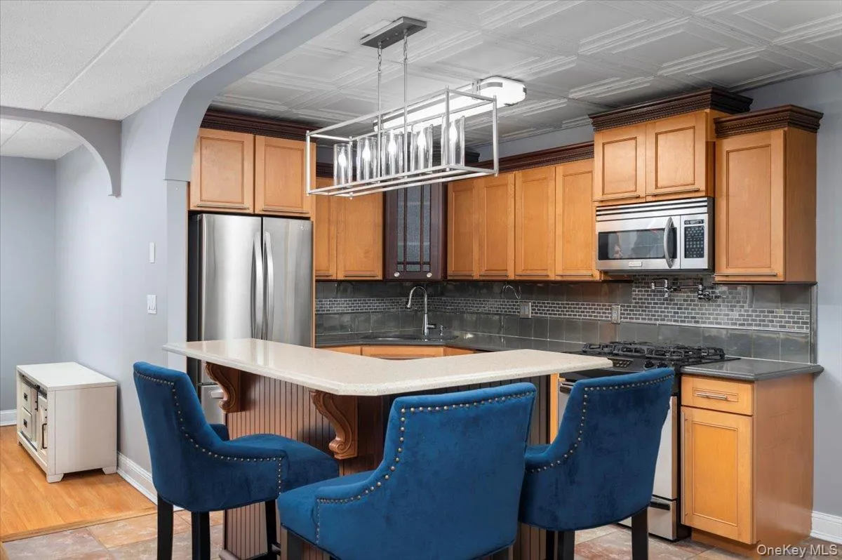 Kitchen featuring wood cabinetry, stainless steel appliances, a tiled backsplash, and an arched entry Kitchen featuring wood cabinetry, stainless steel appliances, a tiled backsplash, and an arched entry
