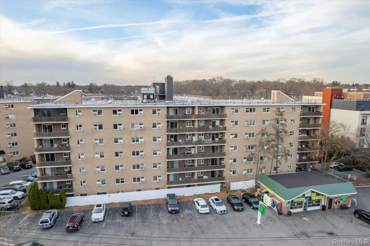 Multi-story residential building featuring balconies and a surrounding paved parking area Multi-story residential building featuring balconies and a surrounding paved parking area