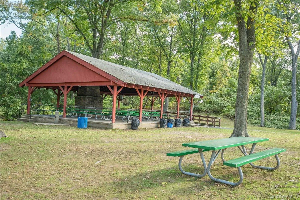 Red-painted open-air pavilion for rent to host parties featuring a central stone structure and multiple picnic tables Red-painted open-air pavilion for rent to host parties featuring a central stone structure and multiple picnic tables