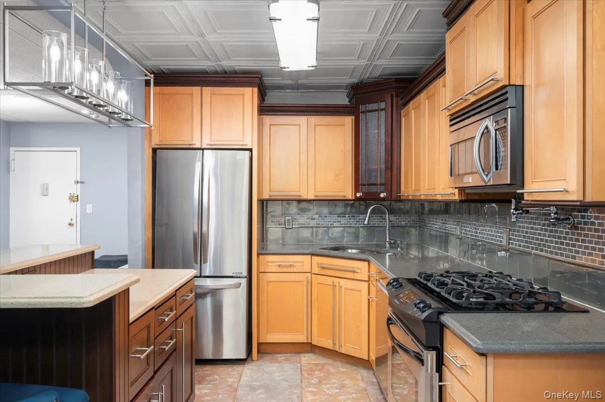 Kitchen featuring wood cabinetry, stainless steel appliances, and a mosaic tile backsplash Kitchen featuring wood cabinetry, stainless steel appliances, and a mosaic tile backsplash