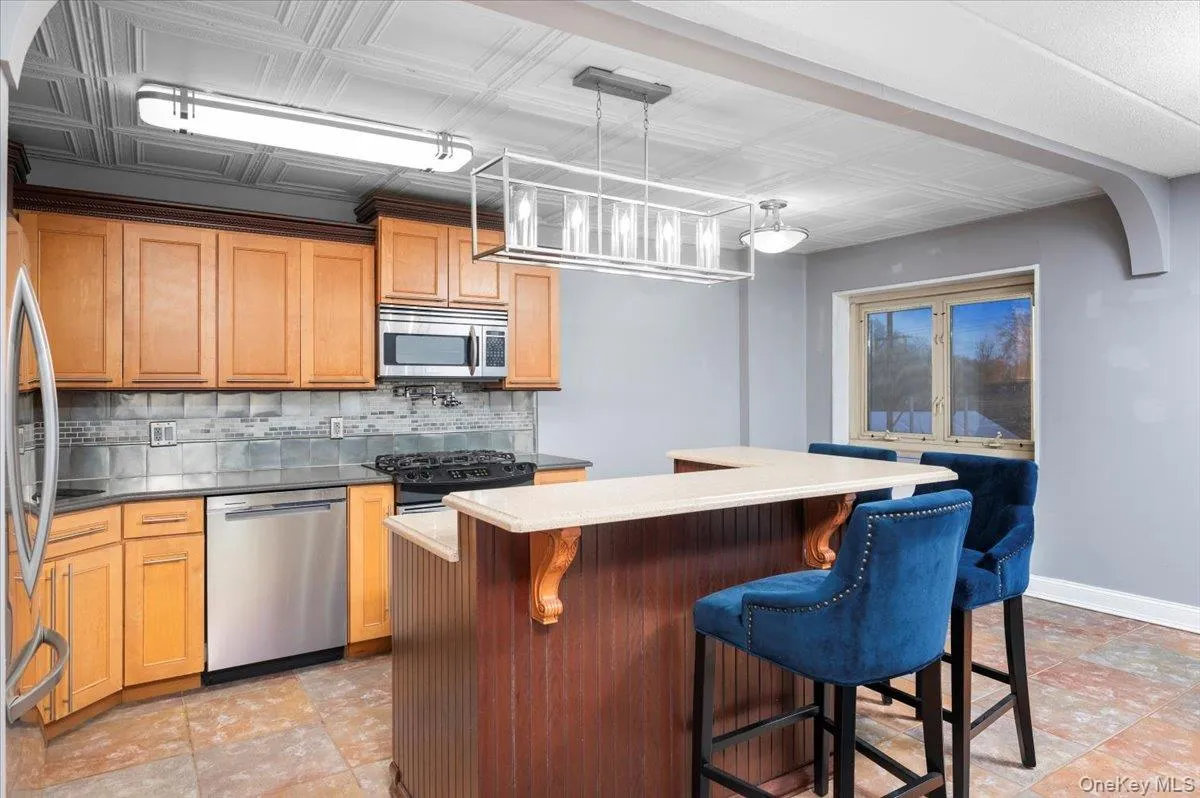 Kitchen featuring stainless steel appliances, wood-finish cabinetry, tile backsplash, and an eat-at island with corbel accents Kitchen featuring stainless steel appliances, wood-finish cabinetry, tile backsplash, and an eat-at island with corbel accents