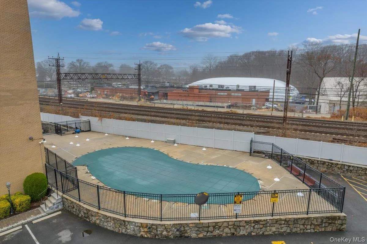 Kidney-shaped outdoor pool with a dark green cover, surrounded by a black metal fence atop a stone wall Kidney-shaped outdoor pool with a dark green cover, surrounded by a black metal fence atop a stone wall