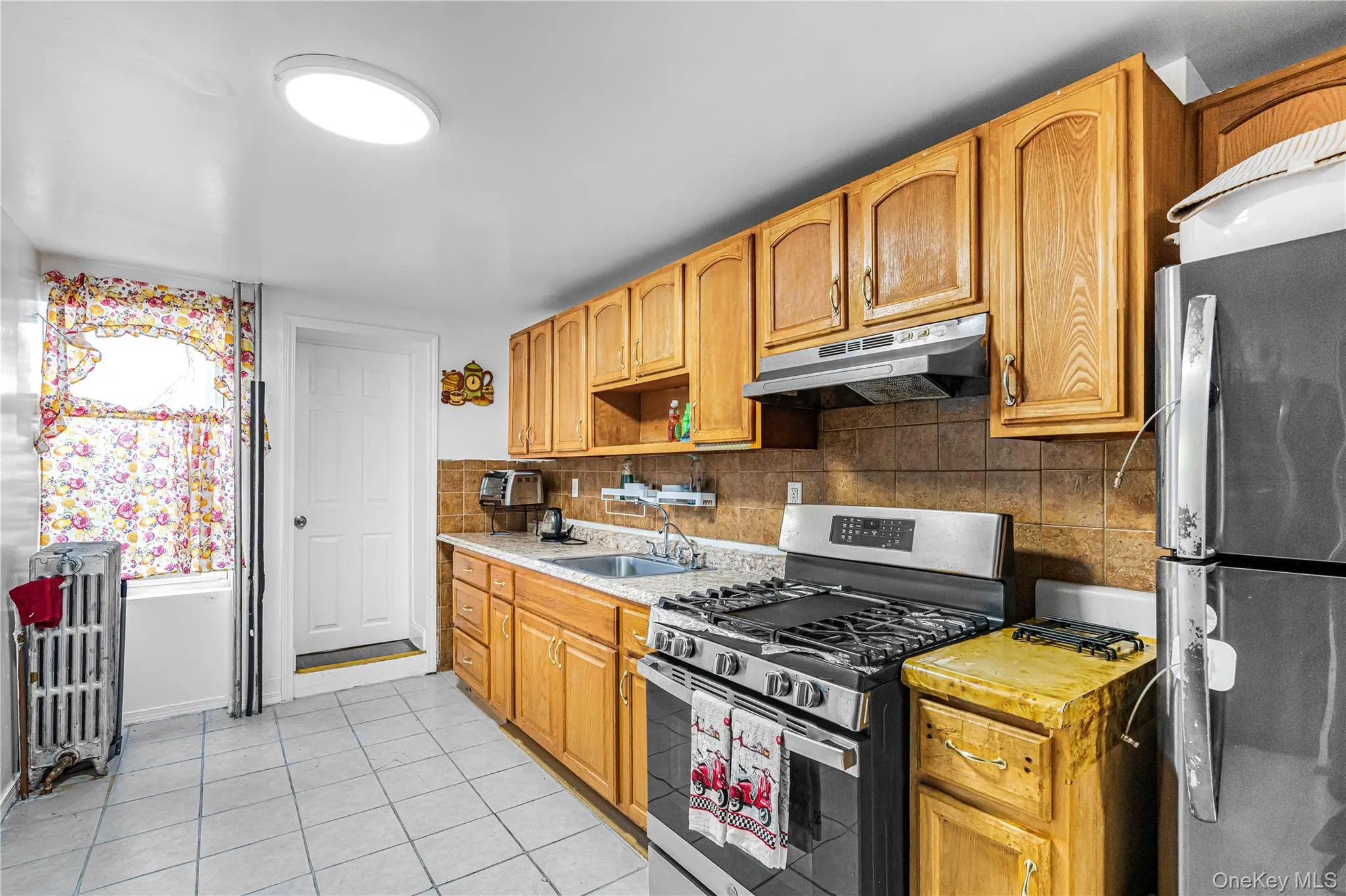 Kitchen featuring light wood cabinetry, stainless steel range with overhead ventilation, and a tiled backsplash Kitchen featuring light wood cabinetry, stainless steel range with overhead ventilation, and a tiled backsplash