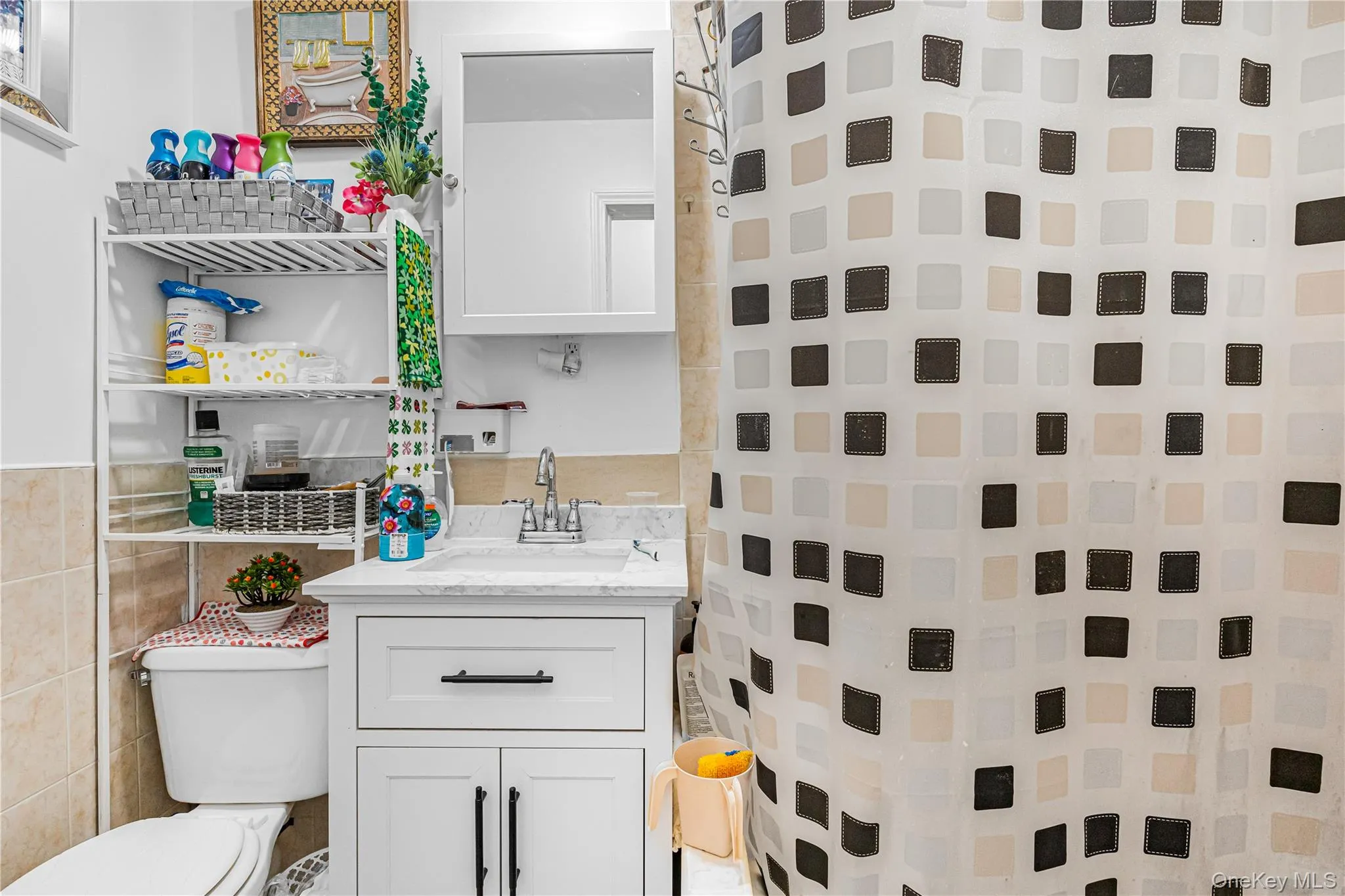 Bathroom featuring a white vanity with paneling and dark hardware, a stone-finish countertop, and a chrome-finish faucet Bathroom featuring a white vanity with paneling and dark hardware, a stone-finish countertop, and a chrome-finish faucet