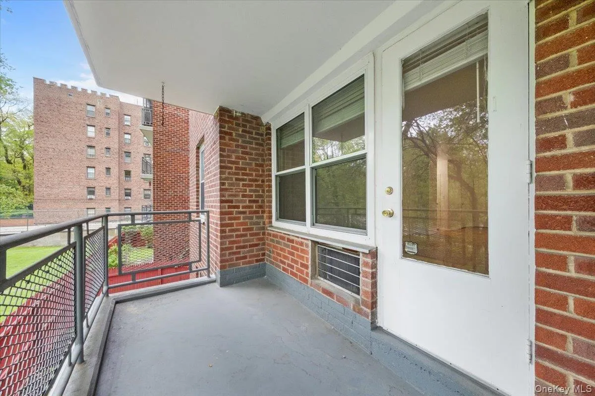 Private balcony featuring a painted concrete floor, brick wall accents, and a metal railing Private balcony featuring a painted concrete floor, brick wall accents, and a metal railing