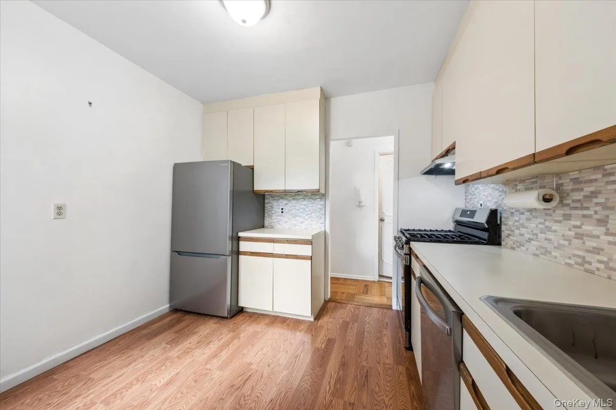 Galley kitchen featuring wood-finish flooring, white cabinetry, light countertops, and a tiled backsplash Galley kitchen featuring wood-finish flooring, white cabinetry, light countertops, and a tiled backsplash