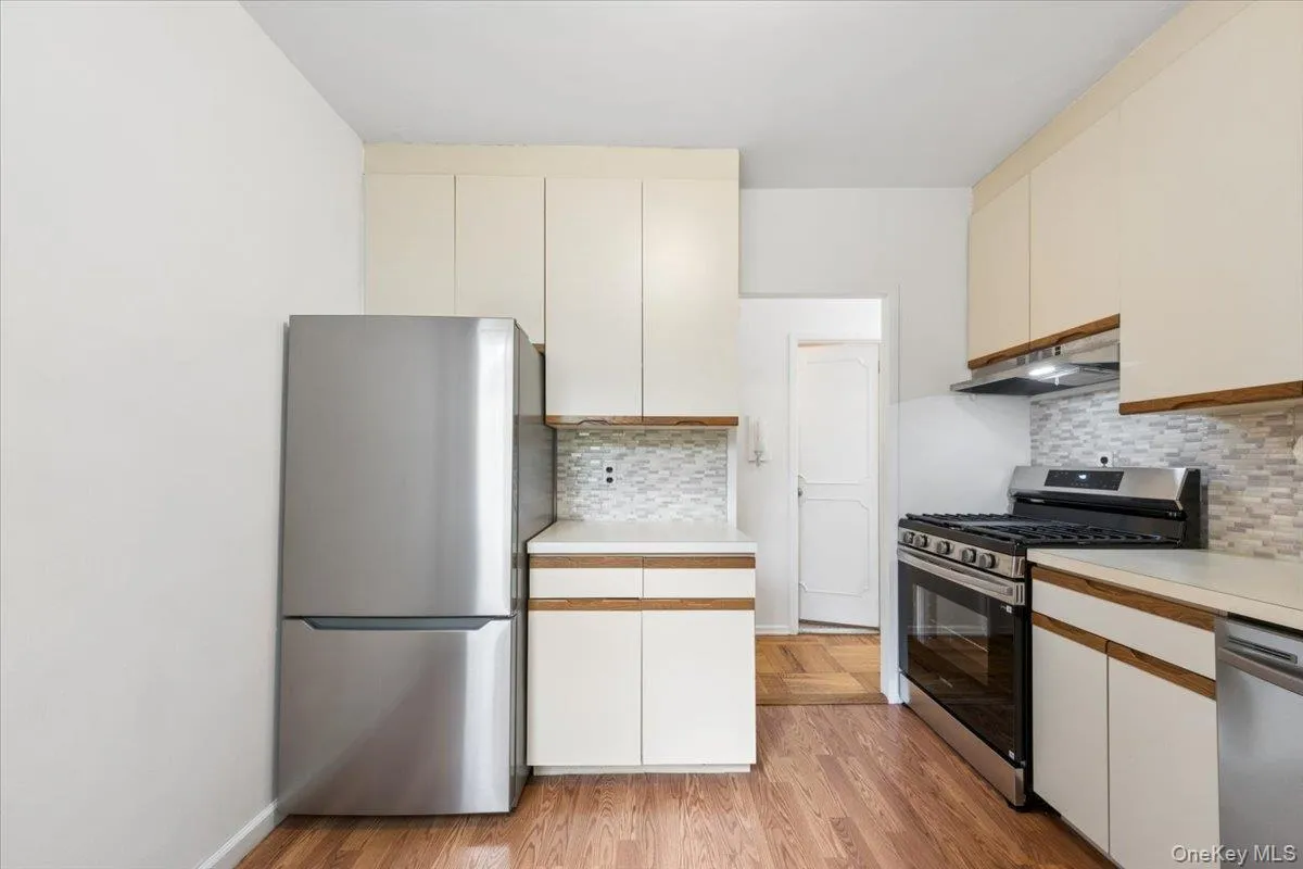 Kitchen featuring stainless steel appliances, upper and lower cabinetry with wood-finish accents, composite countertops, and a tiled backsplash Kitchen featuring stainless steel appliances, upper and lower cabinetry with wood-finish accents, composite countertops, and a tiled backsplash