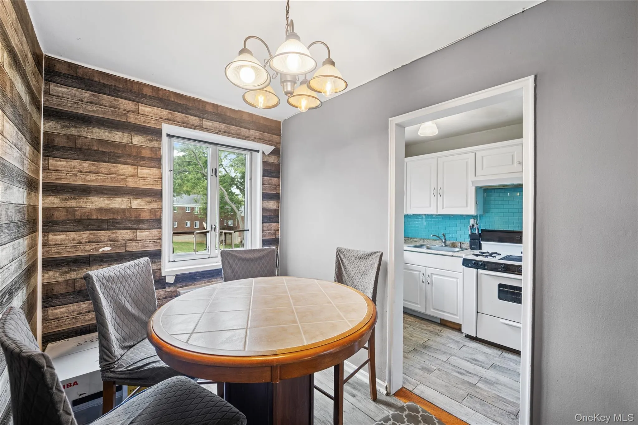 Dining area featuring a wood-panel accent wall, overhead chandelier, and a large window Dining area featuring a wood-panel accent wall, overhead chandelier, and a large window