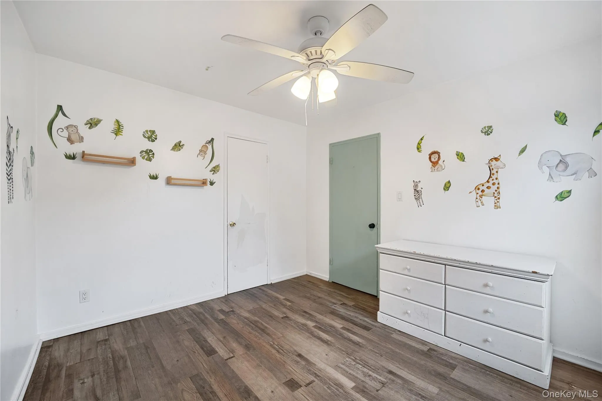 Interior room featuring wood-finish flooring, white walls, and a ceiling fan with integrated lighting Interior room featuring wood-finish flooring, white walls, and a ceiling fan with integrated lighting
