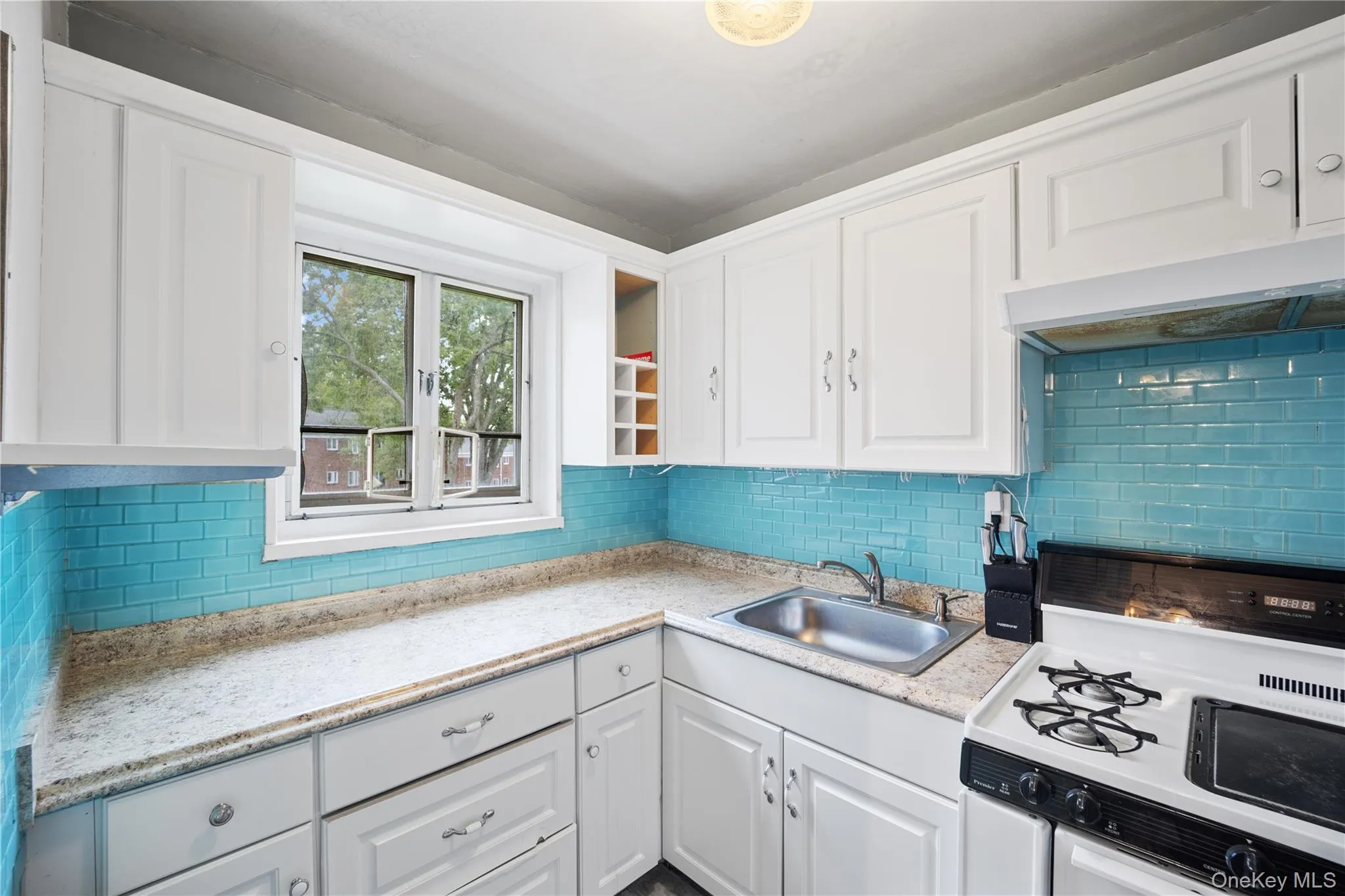 Kitchen featuring white cabinetry, light-toned countertops, a stainless steel sink, and a blue subway tile backsplash Kitchen featuring white cabinetry, light-toned countertops, a stainless steel sink, and a blue subway tile backsplash