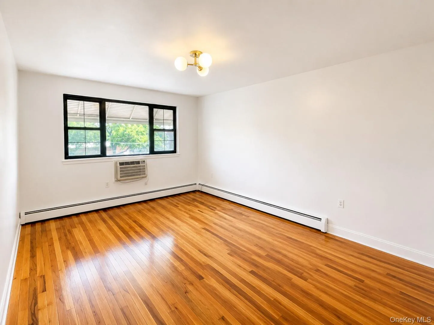 Spacious room featuring wood-finish flooring, white walls, and baseboard heating Spacious room featuring wood-finish flooring, white walls, and baseboard heating