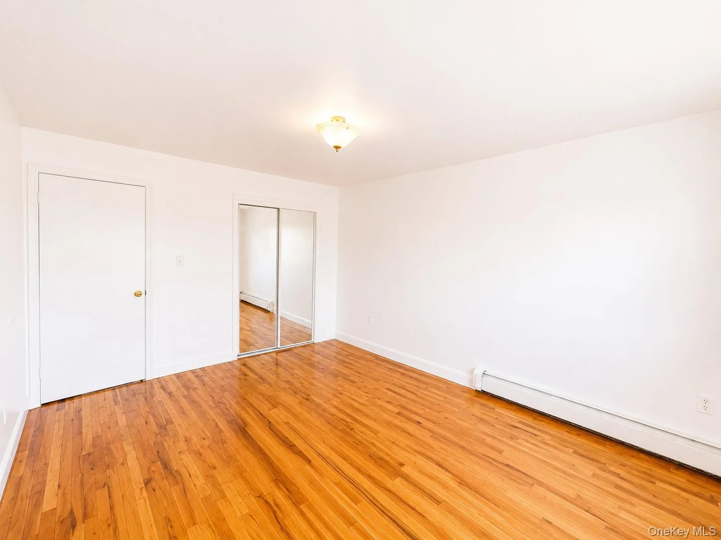 Hardwood flooring throughout, white walls, and a ceiling-mounted light fixture Hardwood flooring throughout, white walls, and a ceiling-mounted light fixture