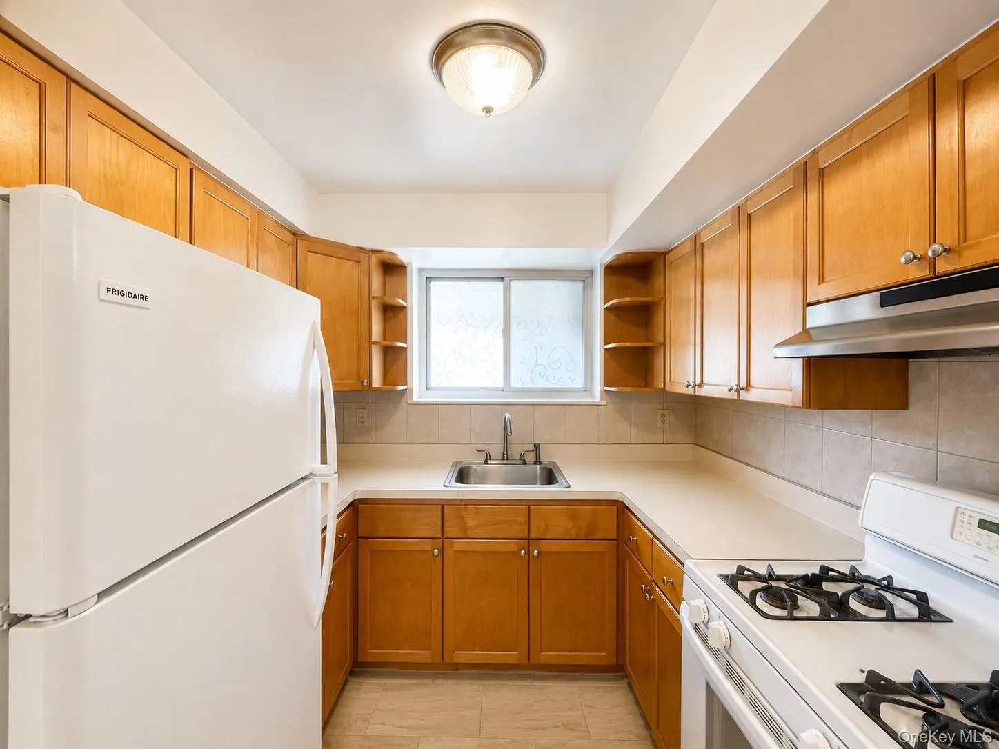 U-shaped kitchen featuring wood cabinetry, solid surface countertops, tile flooring, and a stainless steel sink U-shaped kitchen featuring wood cabinetry, solid surface countertops, tile flooring, and a stainless steel sink