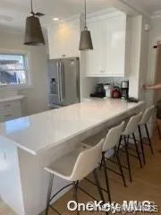 Kitchen with white cabinets, ornamental molding, a peninsula, stainless steel fridge, and decorative light fixtures Kitchen with white cabinets, ornamental molding, a peninsula, stainless steel fridge, and decorative light fixtures