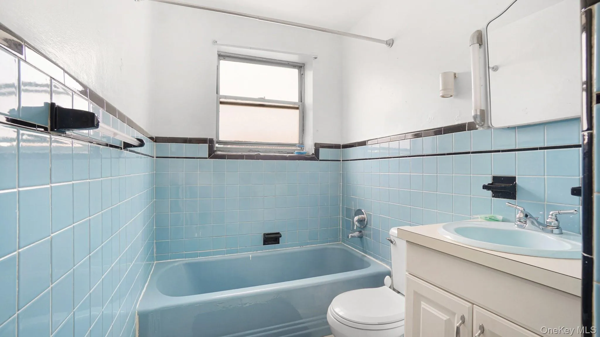 Bathroom featuring light blue wall tiles with a dark accent border, a matching light blue bathtub, and a window Bathroom featuring light blue wall tiles with a dark accent border, a matching light blue bathtub, and a window