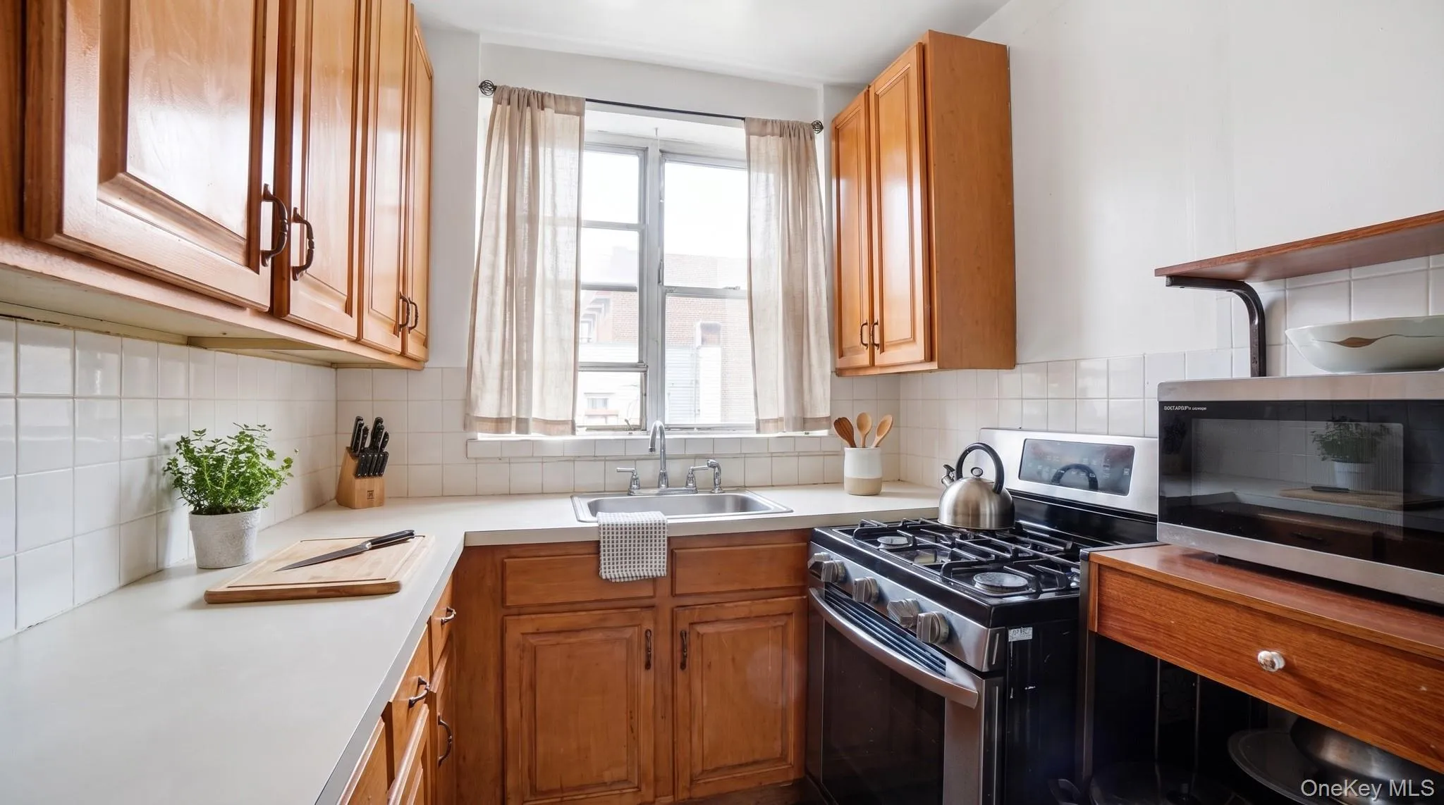 Kitchen featuring wood cabinetry, white countertops, white square tile backsplash, and a stainless steel gas range Kitchen featuring wood cabinetry, white countertops, white square tile backsplash, and a stainless steel gas range