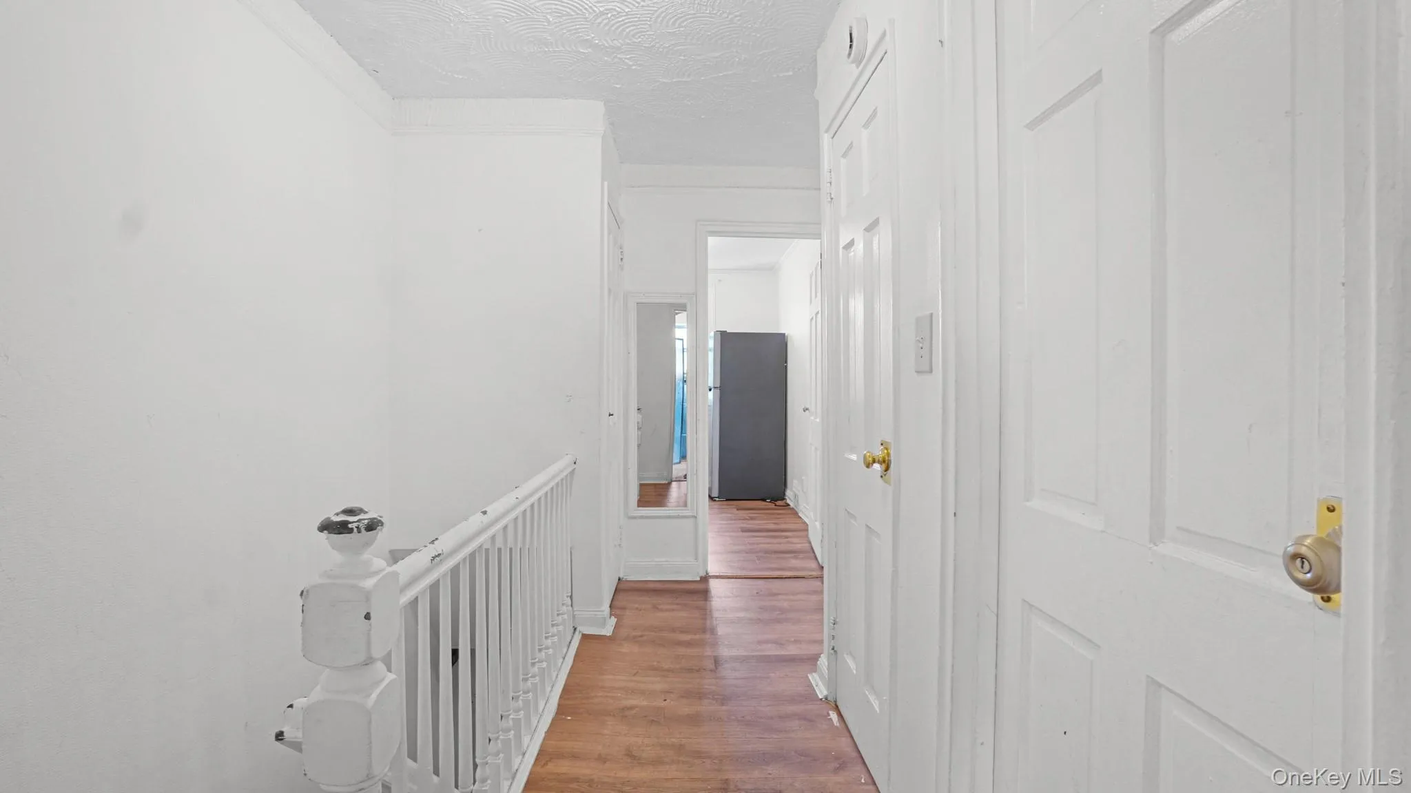Upper-level hallway featuring wood-finish flooring, white paneled doors, and a white painted banister Upper-level hallway featuring wood-finish flooring, white paneled doors, and a white painted banister
