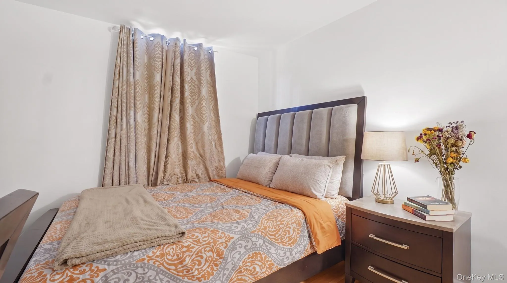 Bright room featuring a paneled upholstered headboard, white walls, and a window with patterned drapes Bright room featuring a paneled upholstered headboard, white walls, and a window with patterned drapes