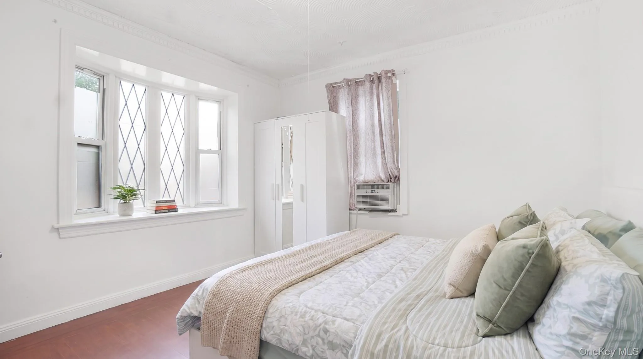 Spacious room featuring a large bay window with decorative muntins, white trim, wood-finish flooring, and crown molding Spacious room featuring a large bay window with decorative muntins, white trim, wood-finish flooring, and crown molding