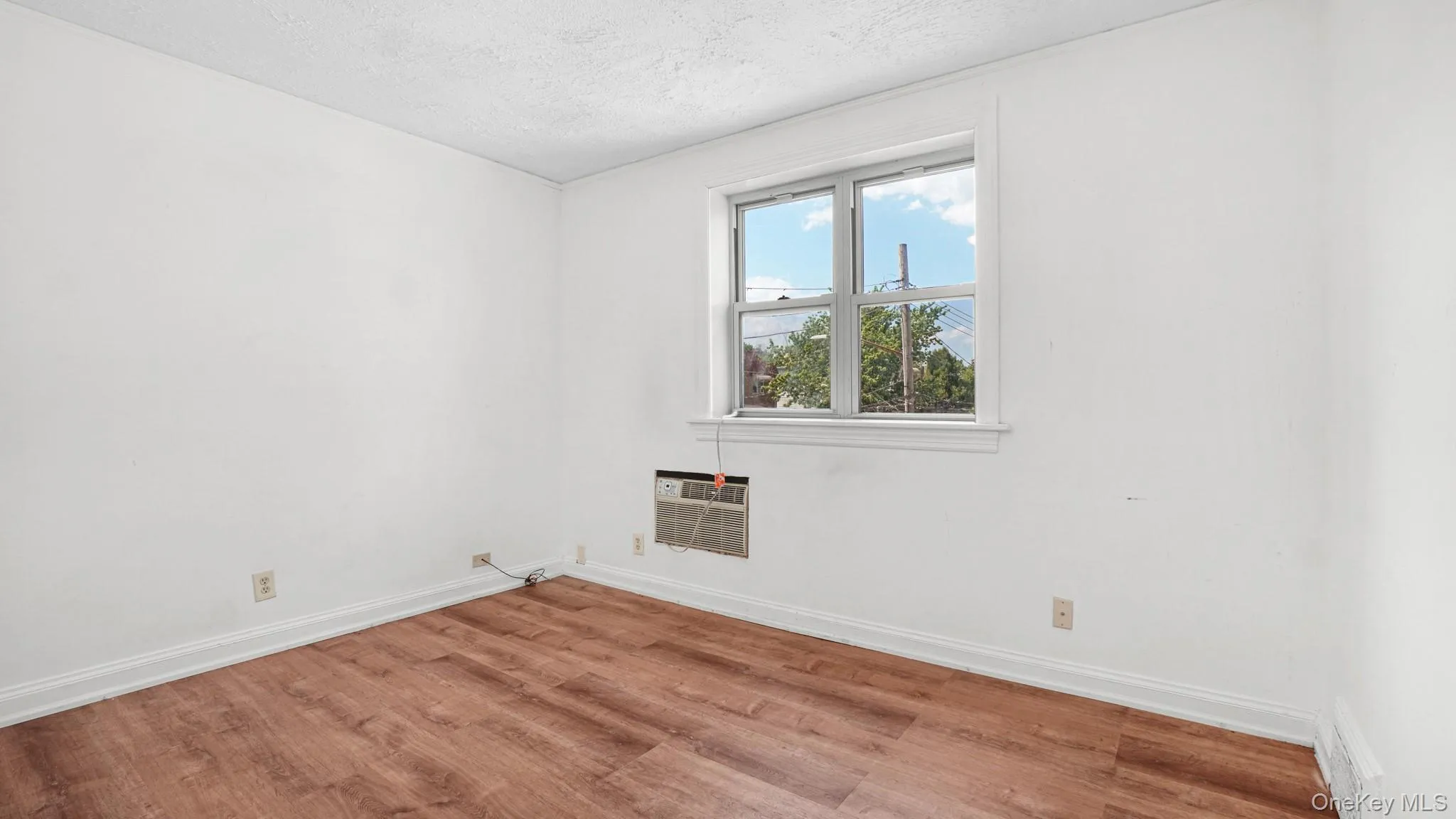 Neutral interior room featuring wood-finish flooring, white baseboards, and a window with white trim Neutral interior room featuring wood-finish flooring, white baseboards, and a window with white trim