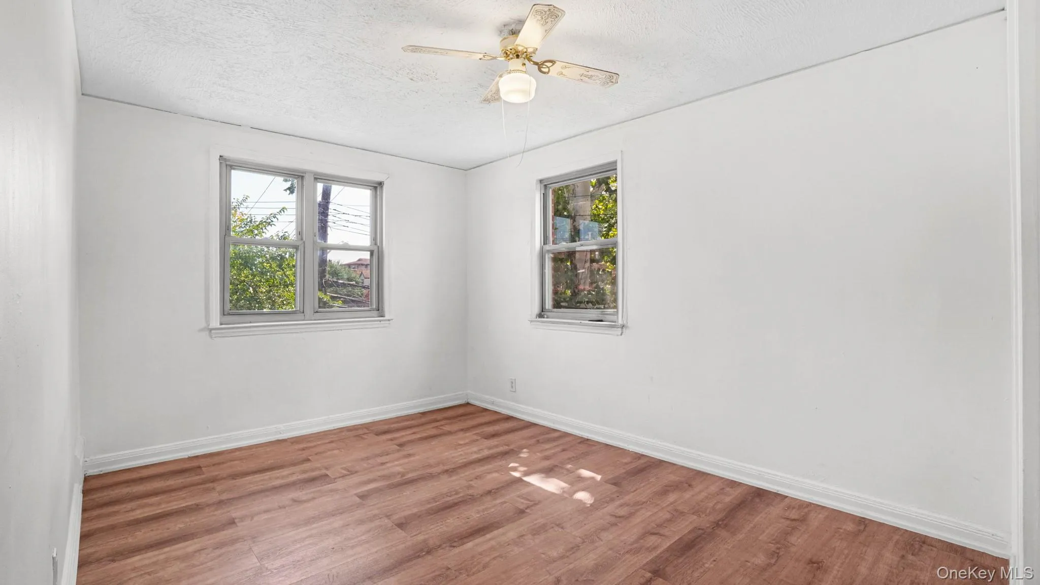 Interior space featuring wood-finish flooring, two large windows, white walls, and a ceiling fan Interior space featuring wood-finish flooring, two large windows, white walls, and a ceiling fan