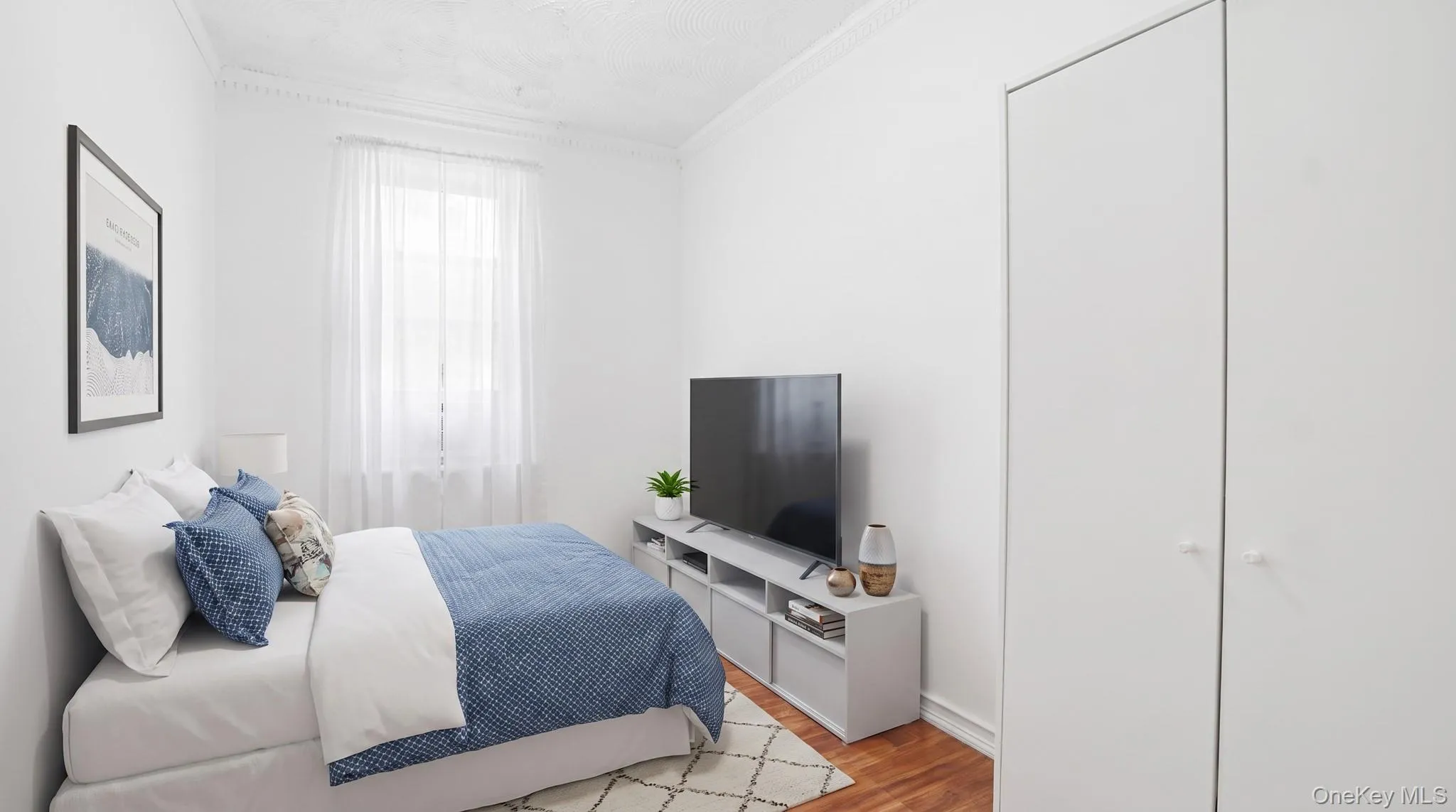 Bedroom featuring hardwood-finish flooring, a window with sheer curtains, white walls, and built-in closet doors Bedroom featuring hardwood-finish flooring, a window with sheer curtains, white walls, and built-in closet doors