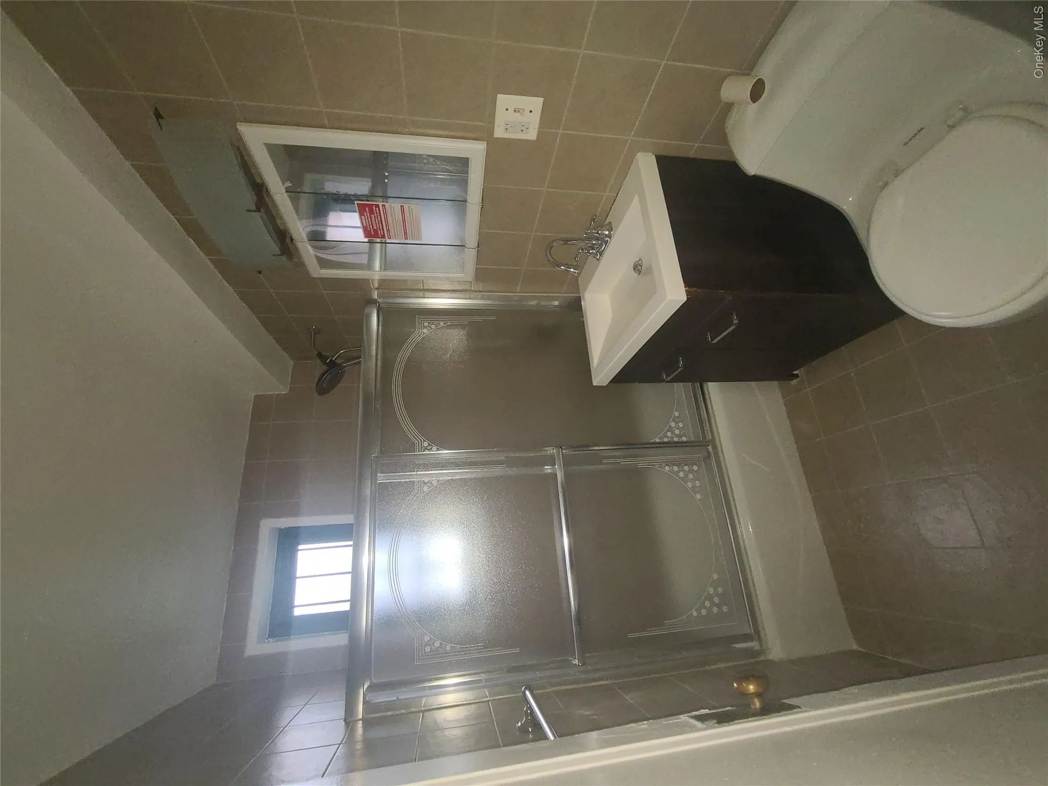 Full bathroom with shower / bath combination with glass door, tile walls, tile patterned flooring, vanity, and toilet Full bathroom with shower / bath combination with glass door, tile walls, tile patterned flooring, vanity, and toilet