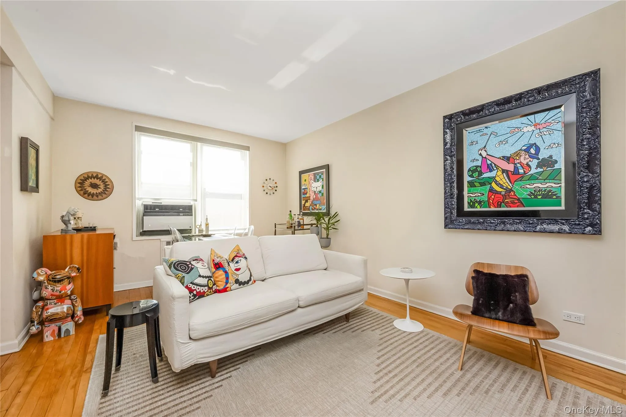 Bright living area featuring wood-finish flooring, light neutral wall tones, and a large window Bright living area featuring wood-finish flooring, light neutral wall tones, and a large window